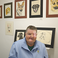 Photograph of Christine at previous exhibition with her pictures hung on the wall behind her