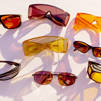 Photo shows several pairs of sunglasses on a table with sunlight shining through