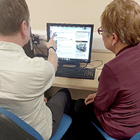 Photo of two people in front of a computer having a conversation