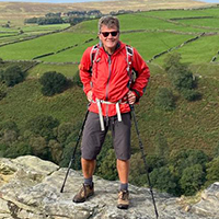Photo of Rob in walking gear standing on a stone with a view of rolling hills behind him