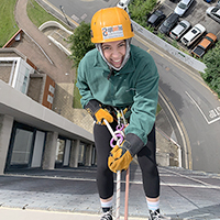 Photo os someone doing an abseil, looking at them over the side of a building and the street below them