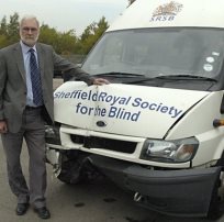 Photograph of damaged minibus with Steve Hambleton stood alongside looking very upset