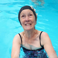 Photo of someone in a swimming pool smiling and wearing a swimming hat 