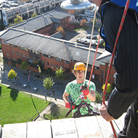Photo taken from above of someone abseiling down the side of the Owen Building in Sheffield. The view looks down on some smaller buildings
